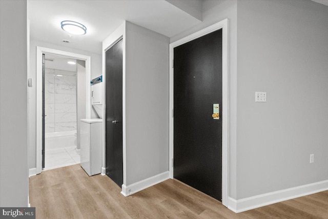 corridor featuring stacked washer / drying machine and light hardwood / wood-style flooring