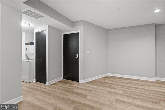 spare room featuring stacked washer / drying machine and light hardwood / wood-style flooring