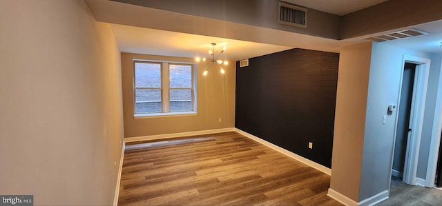 empty room featuring wood-type flooring and a chandelier