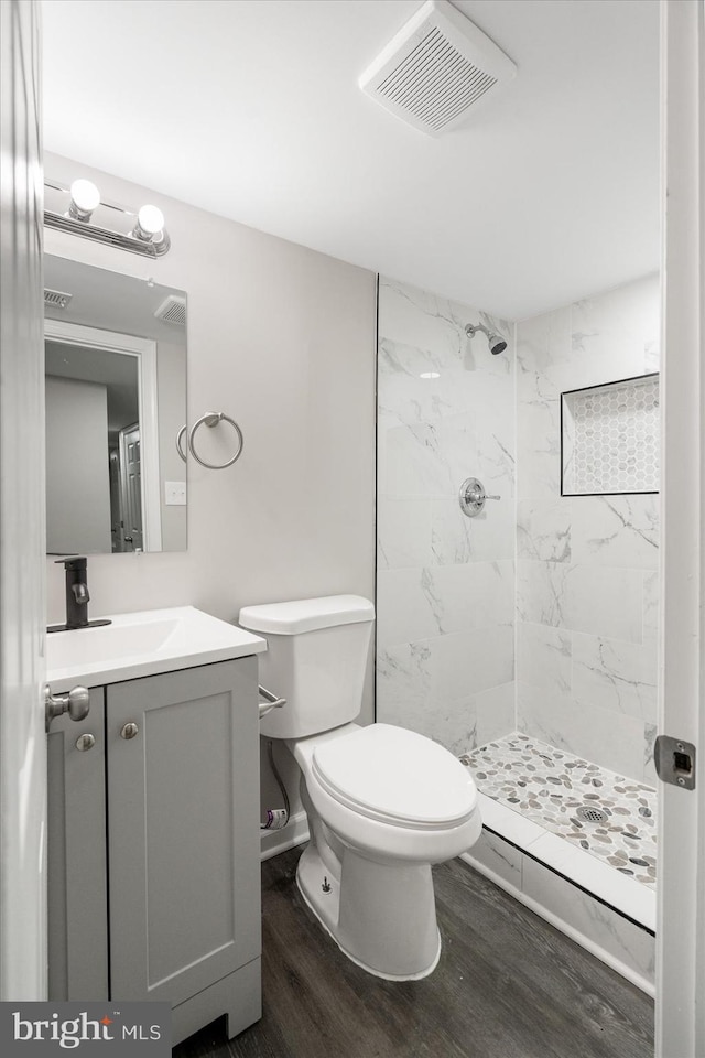 bathroom featuring vanity, hardwood / wood-style floors, toilet, and tiled shower