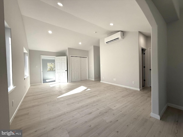 unfurnished living room featuring lofted ceiling, a wall mounted air conditioner, and light hardwood / wood-style floors