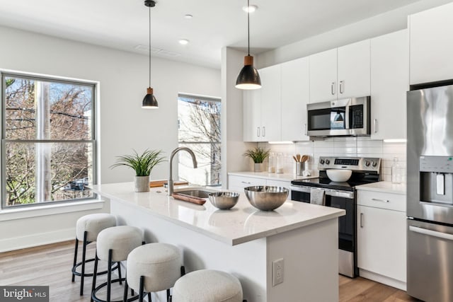 kitchen with appliances with stainless steel finishes, decorative light fixtures, light stone countertops, and a center island with sink