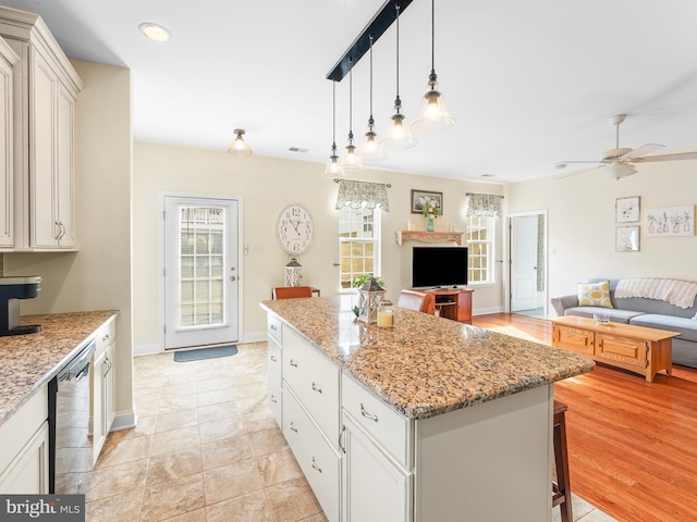 kitchen with stainless steel dishwasher, a kitchen island, pendant lighting, light stone countertops, and white cabinets