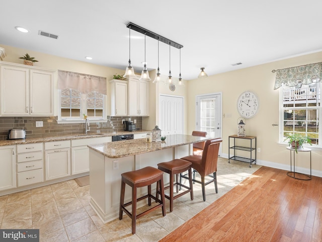 kitchen featuring a kitchen island, decorative light fixtures, sink, backsplash, and light stone countertops