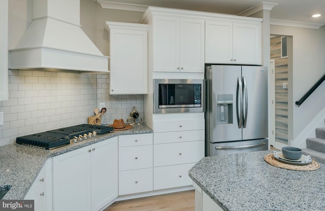 kitchen featuring premium range hood, ornamental molding, appliances with stainless steel finishes, and white cabinets