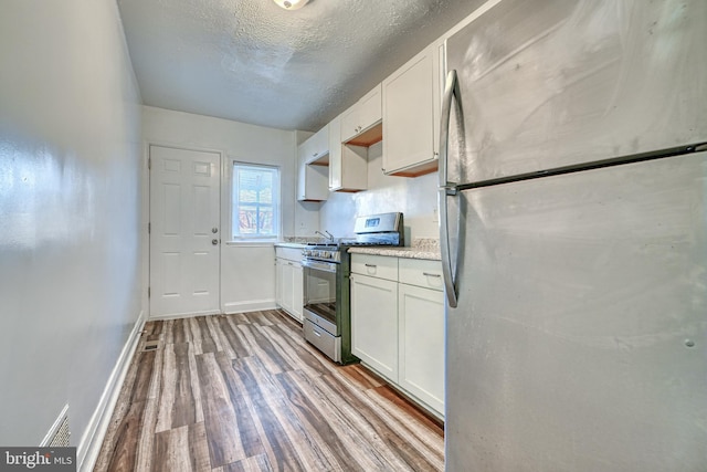 kitchen featuring white cabinetry, stainless steel appliances, a textured ceiling, and light wood-type flooring