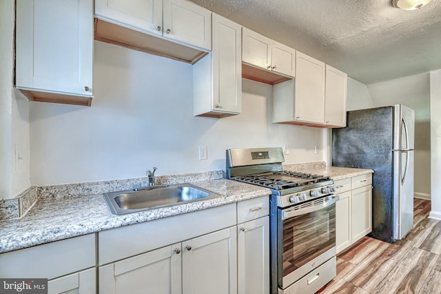 kitchen with appliances with stainless steel finishes, white cabinetry, sink, a textured ceiling, and light hardwood / wood-style flooring