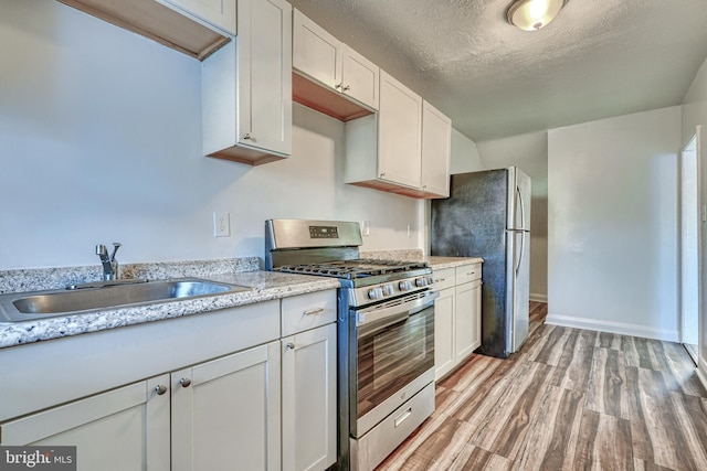 kitchen with sink, stainless steel appliances, a textured ceiling, white cabinets, and light wood-type flooring