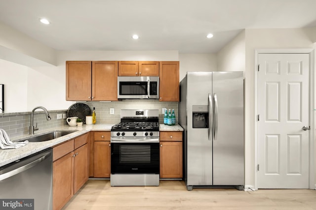 kitchen featuring sink, appliances with stainless steel finishes, light stone countertops, light hardwood / wood-style floors, and backsplash