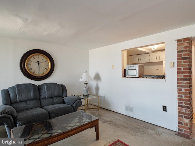 living area featuring unfinished concrete flooring, visible vents, and baseboards