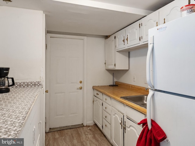 kitchen with light wood finished floors, light countertops, freestanding refrigerator, white cabinetry, and a sink