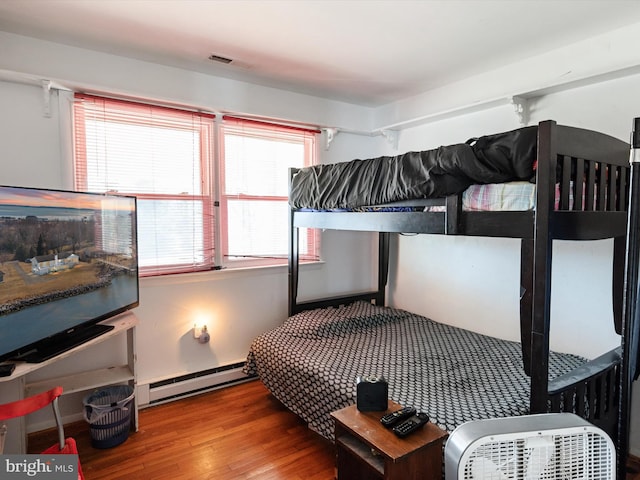 bedroom with a baseboard heating unit, visible vents, and wood finished floors