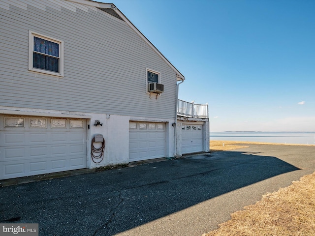 view of property exterior with a garage, a water view, cooling unit, and stucco siding