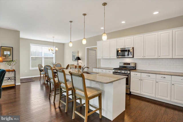 kitchen featuring sink, hanging light fixtures, stainless steel appliances, white cabinets, and a center island with sink