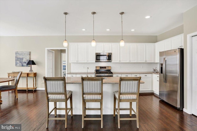 kitchen featuring pendant lighting, white cabinetry, stainless steel appliances, light stone counters, and a center island with sink