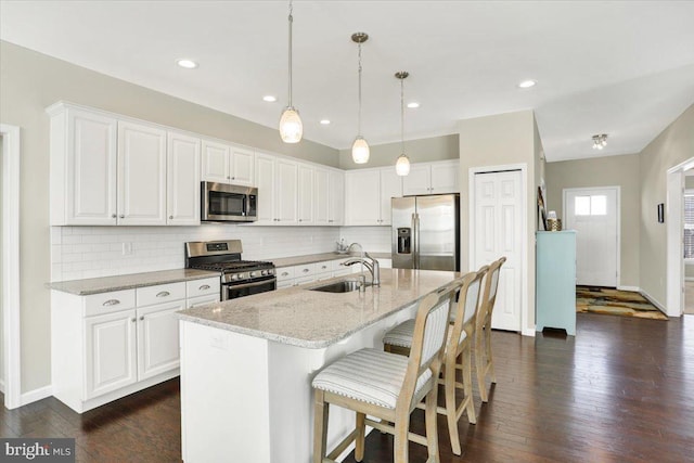 kitchen featuring appliances with stainless steel finishes, sink, white cabinets, a kitchen island with sink, and light stone countertops