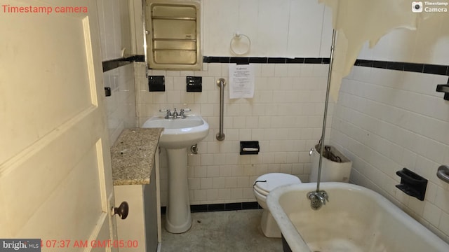 bathroom with a tub to relax in, sink, tile walls, and toilet