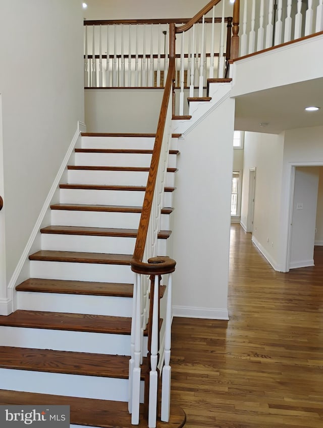 staircase with recessed lighting, a high ceiling, baseboards, and wood finished floors