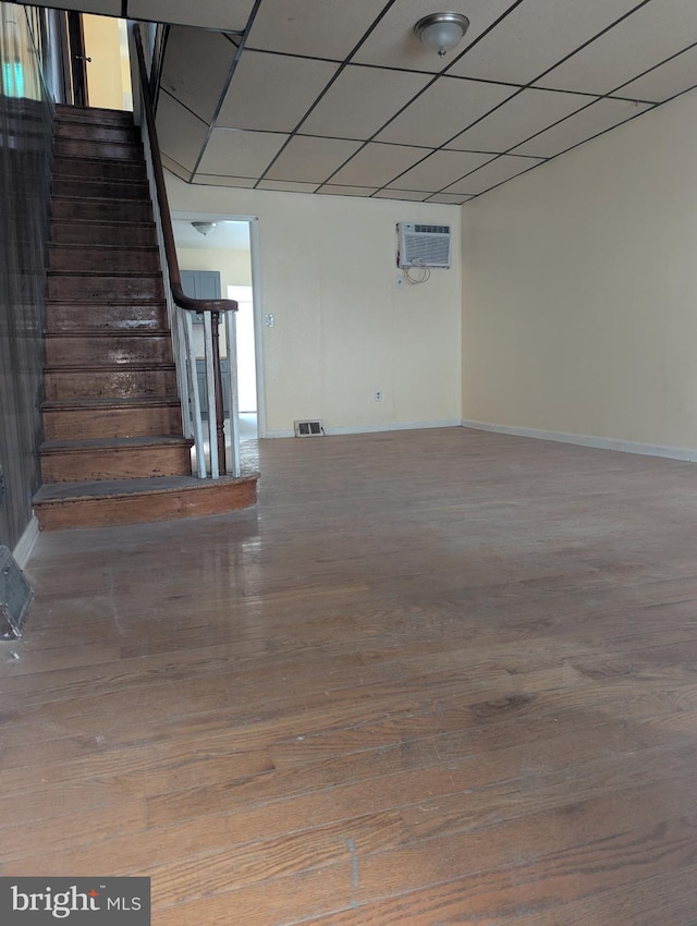 interior space featuring wood-type flooring, a wall mounted air conditioner, and a drop ceiling