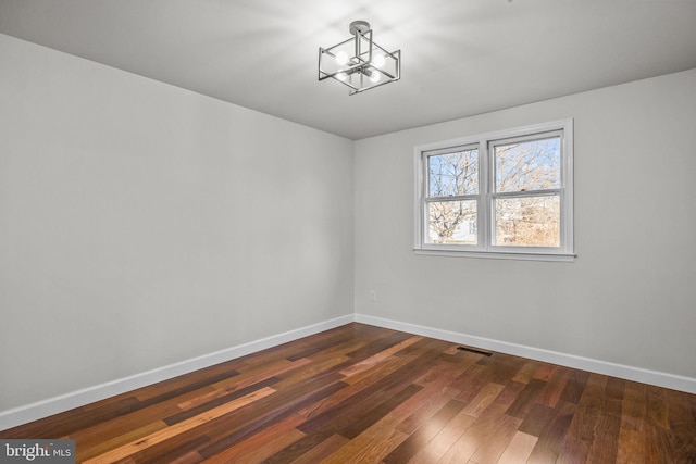 spare room with dark hardwood / wood-style floors and a notable chandelier