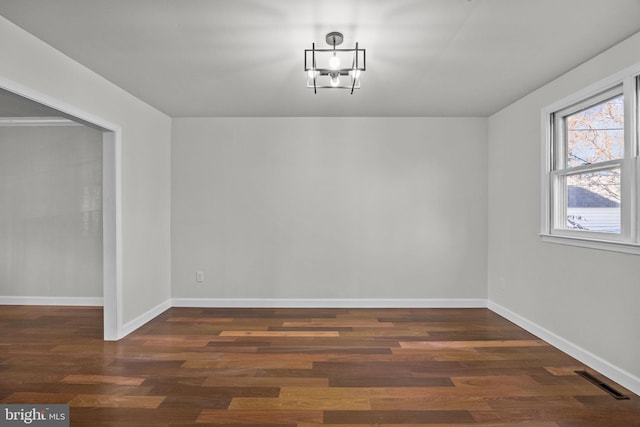 spare room with dark wood-type flooring and a notable chandelier