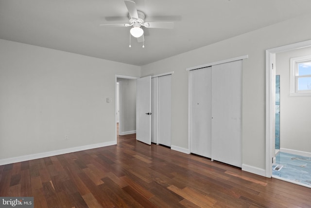 unfurnished bedroom featuring multiple closets, ceiling fan, and dark hardwood / wood-style floors