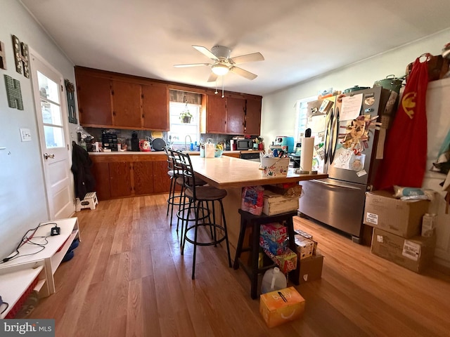 kitchen featuring a breakfast bar, stainless steel refrigerator, kitchen peninsula, light hardwood / wood-style floors, and decorative backsplash