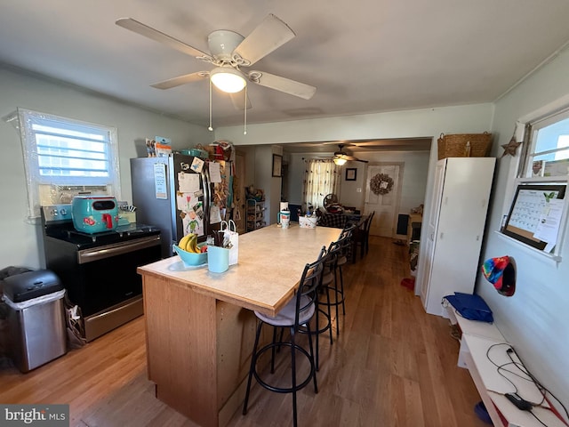 kitchen with a kitchen bar, light hardwood / wood-style floors, ceiling fan, and appliances with stainless steel finishes