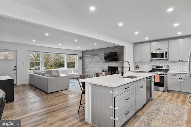 kitchen with sink, a breakfast bar, stainless steel appliances, an island with sink, and a stone fireplace