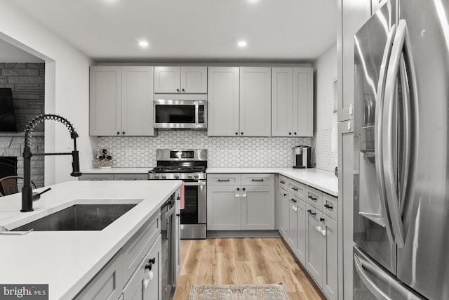 kitchen with sink, gray cabinets, stainless steel appliances, and light wood-type flooring