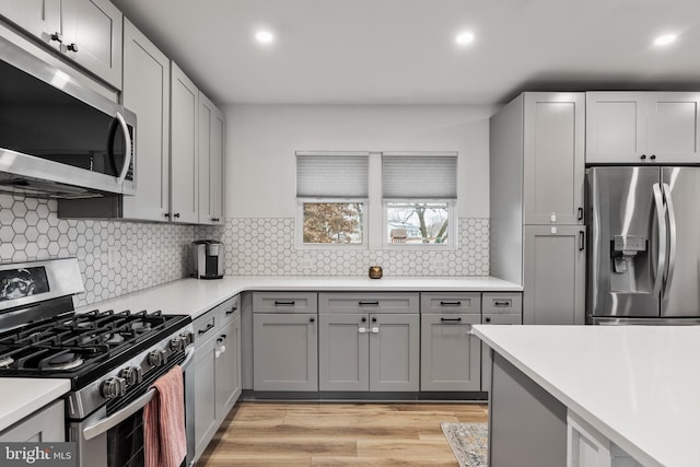 kitchen with stainless steel appliances, gray cabinets, backsplash, and light hardwood / wood-style flooring