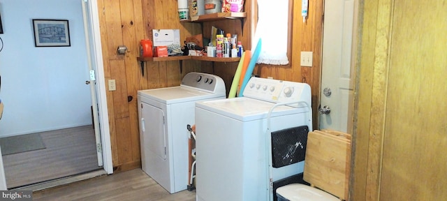 laundry area with light hardwood / wood-style flooring, washer and dryer, and wood walls