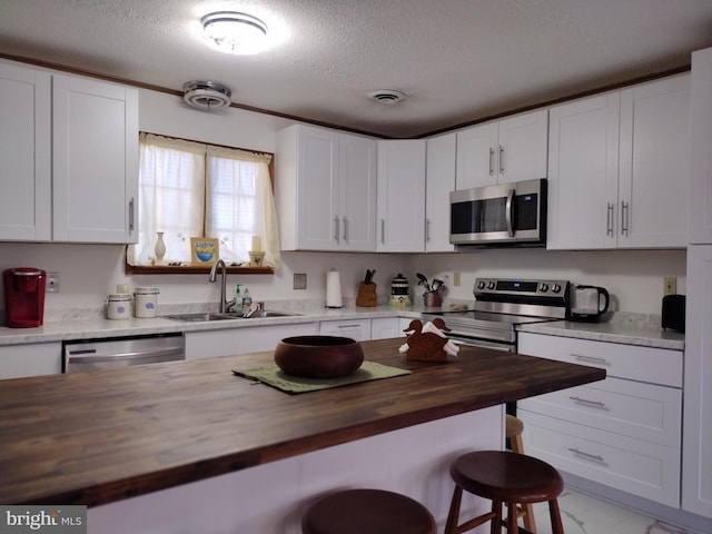 kitchen with sink, appliances with stainless steel finishes, white cabinetry, a kitchen bar, and wood counters