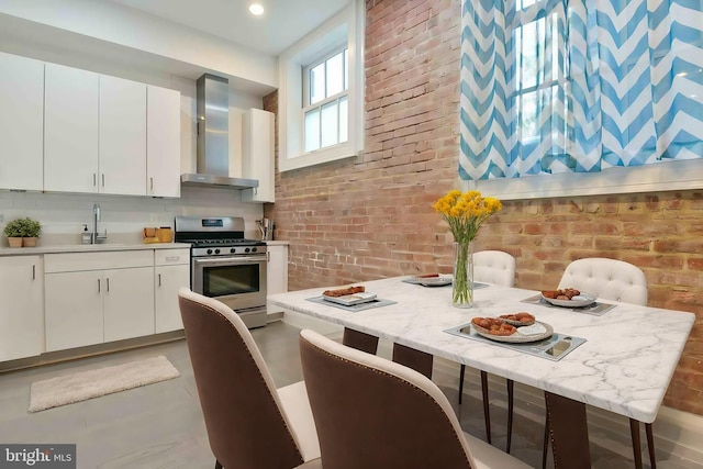 kitchen featuring wall chimney range hood, stainless steel gas range, sink, and white cabinets