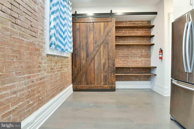 mudroom featuring a barn door, wood-type flooring, and brick wall