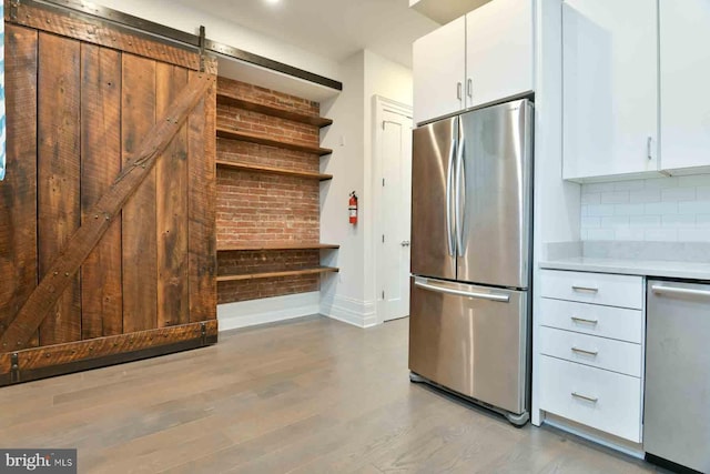 kitchen with appliances with stainless steel finishes, backsplash, white cabinets, a barn door, and light wood-type flooring