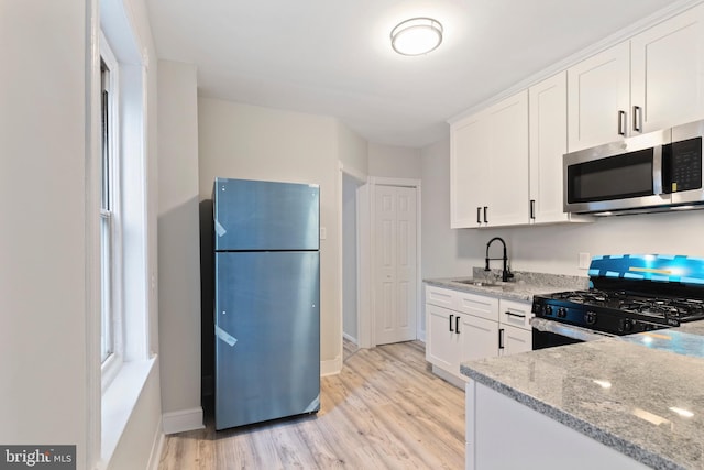 kitchen featuring sink, refrigerator, black range with gas stovetop, light stone countertops, and white cabinets