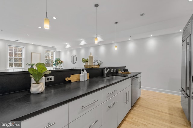 kitchen with sink, white cabinets, hanging light fixtures, stainless steel dishwasher, and light hardwood / wood-style floors