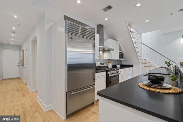 kitchen featuring wall chimney exhaust hood, sink, white cabinetry, built in appliances, and light wood-type flooring