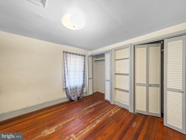 unfurnished bedroom with dark hardwood / wood-style flooring and multiple closets