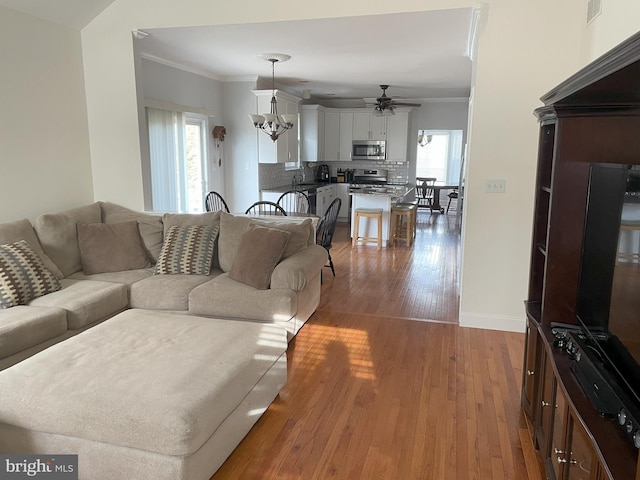 living room featuring ornamental molding, wood-type flooring, and ceiling fan with notable chandelier