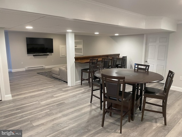 dining area with baseboard heating, indoor bar, wood-type flooring, and ornamental molding