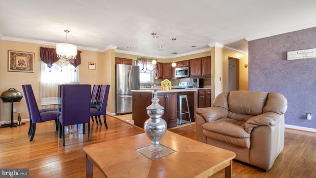 living room with crown molding, a chandelier, and light hardwood / wood-style flooring