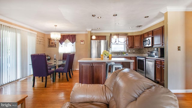 kitchen featuring an inviting chandelier, hanging light fixtures, stainless steel appliances, a center island, and light wood-type flooring