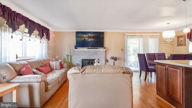 living room with crown molding, a fireplace, light hardwood / wood-style flooring, and a notable chandelier