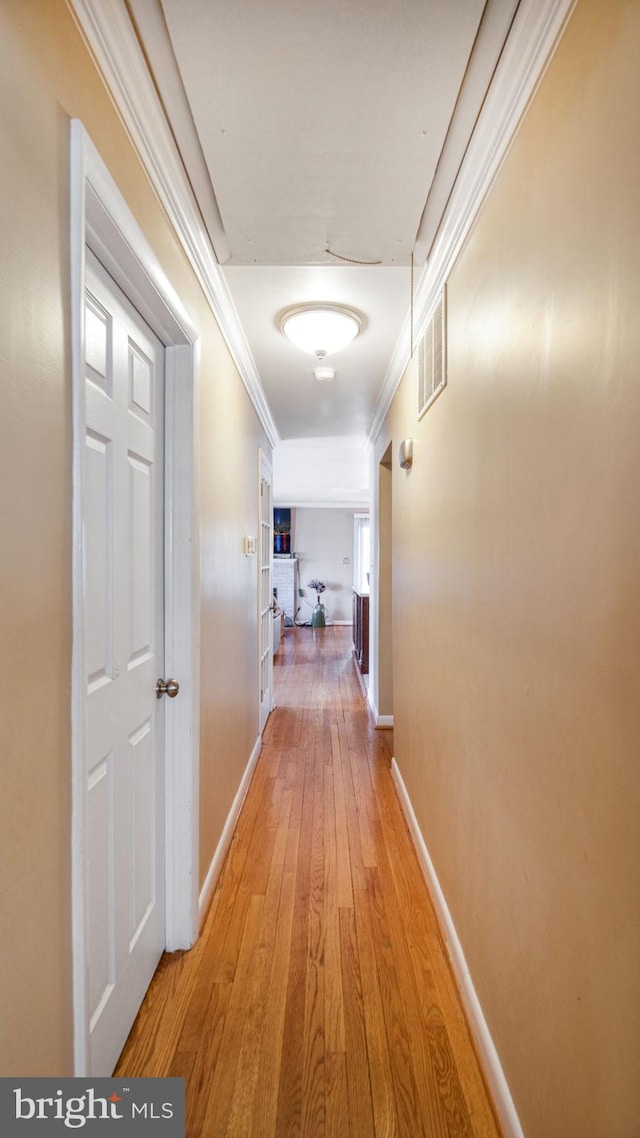 corridor with ornamental molding and light hardwood / wood-style floors