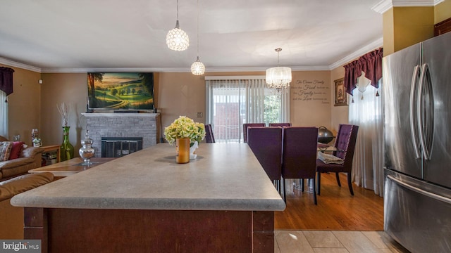 kitchen featuring crown molding, light hardwood / wood-style flooring, a brick fireplace, stainless steel refrigerator, and pendant lighting