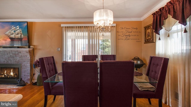 dining space with crown molding, a brick fireplace, hardwood / wood-style floors, and a notable chandelier