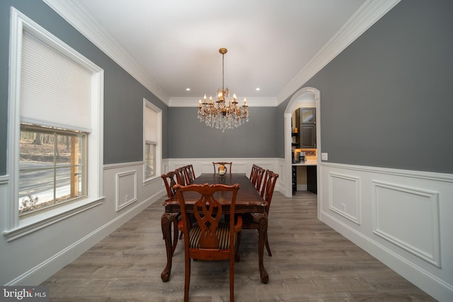 dining room with arched walkways, ornamental molding, wainscoting, wood finished floors, and a chandelier