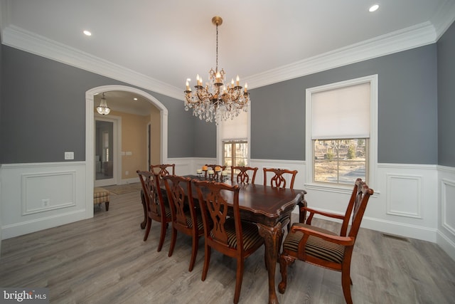 dining room with arched walkways, ornamental molding, wood finished floors, and wainscoting